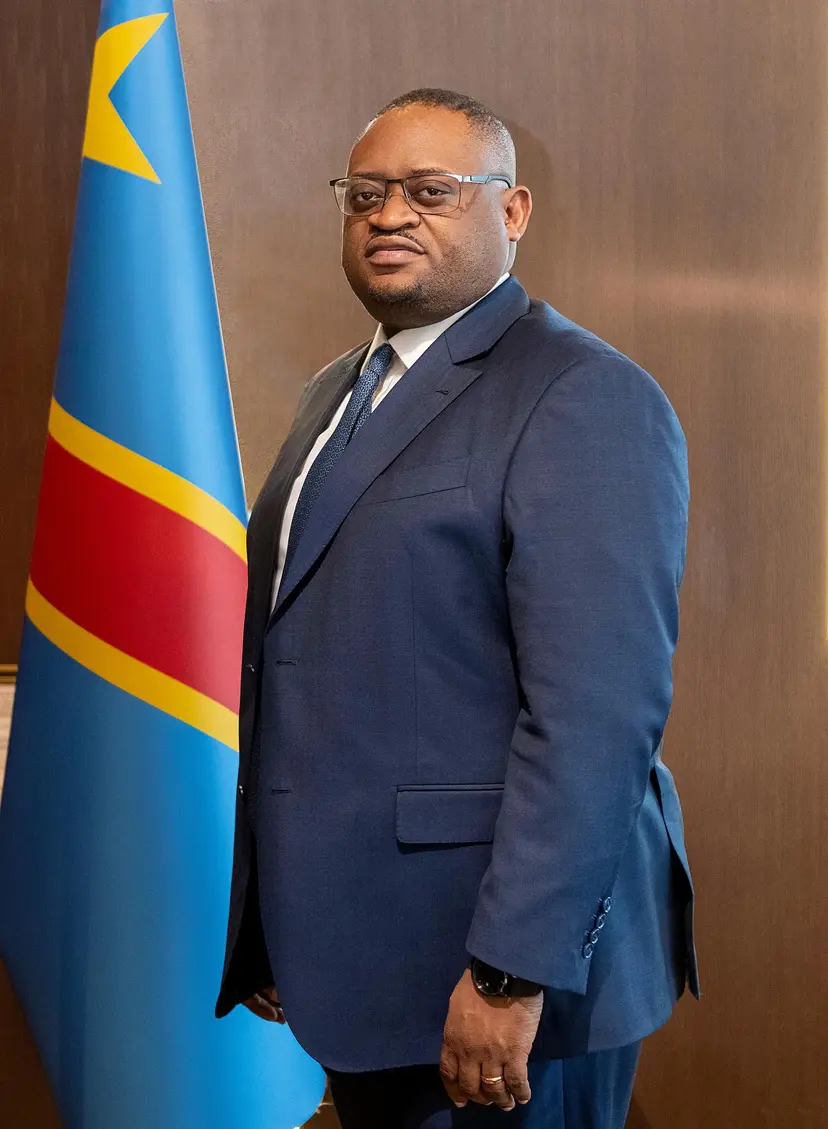 Doudou Fwamba Likunde Li-Botayi, ministre des Finances de la République Démocratique du Congo, posant devant le drapeau national.